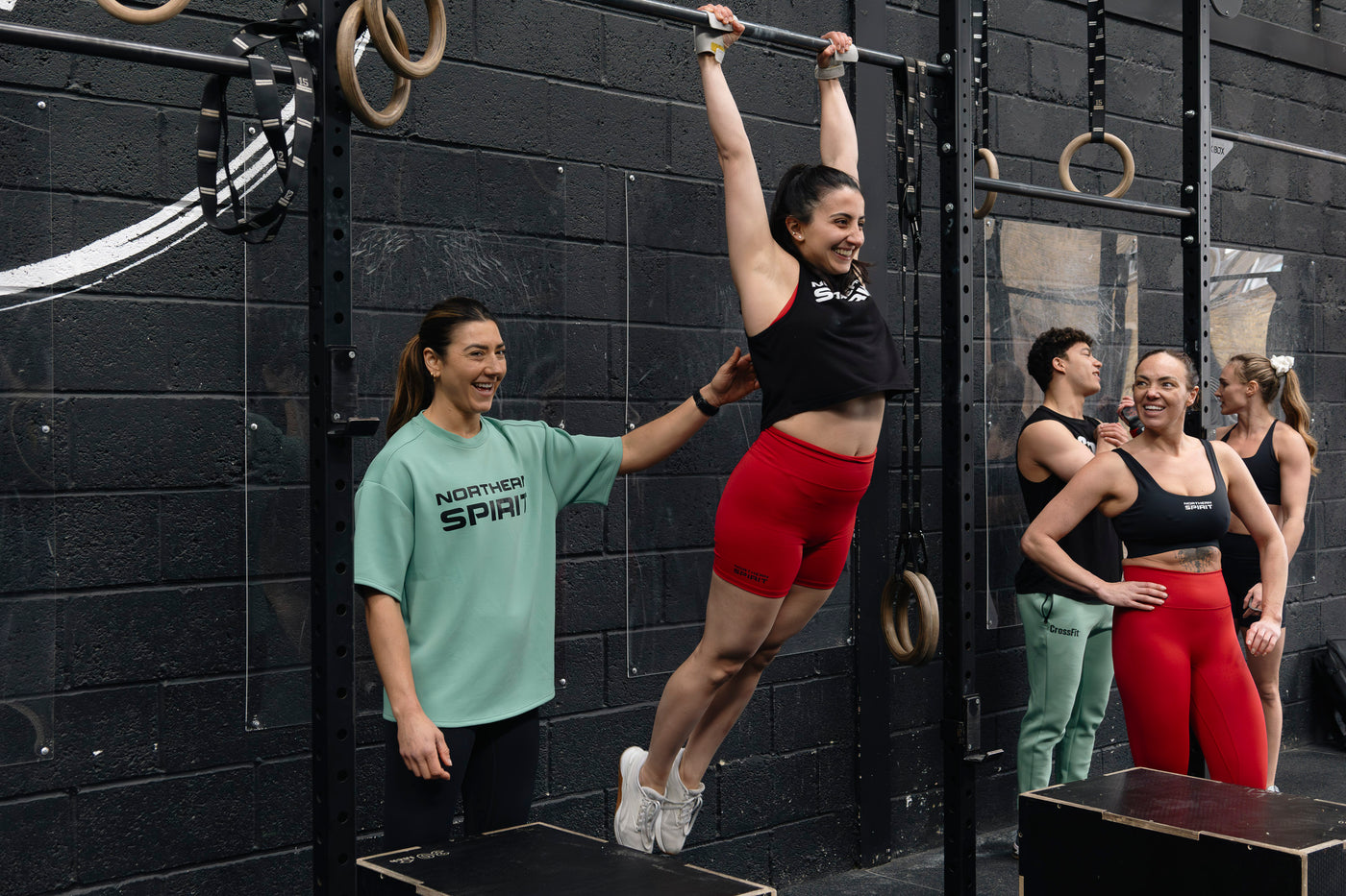 Person performing pull-ups with support from others in a gym setting
