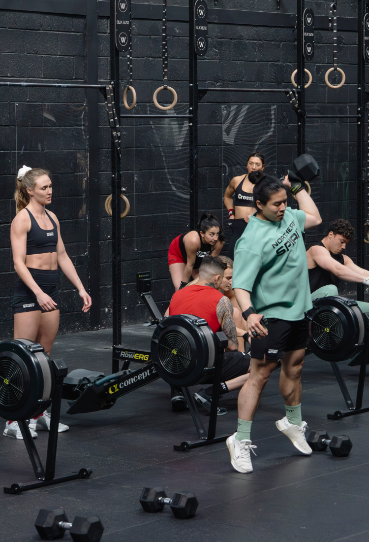 CrossFit® athletes training in a gym wearing Northern Spirit apparel using Concept2 rowers and dumbbells during a functional fitness session.