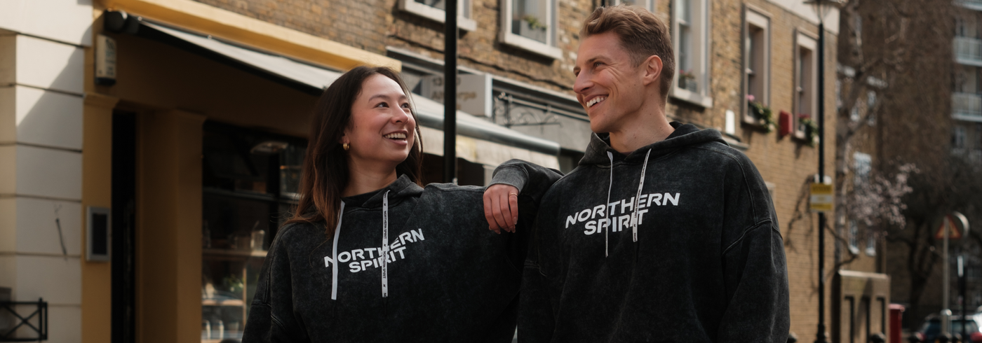 Two athletes wearing Northern Spirit black washed hoodies walking and smiling in the street – Cozy Collection – premium CrossFit and lifestyle apparel made for comfort and recovery.