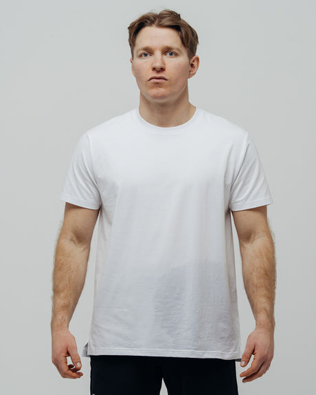 A man wearing a plain white T-shirt and black pants standing against a neutral background.