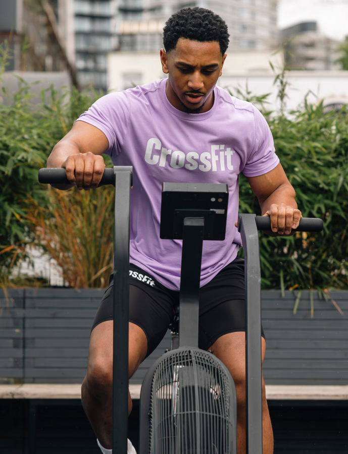 Person wearing a purple CrossFit t-shirt using an exercise bike outdoors.