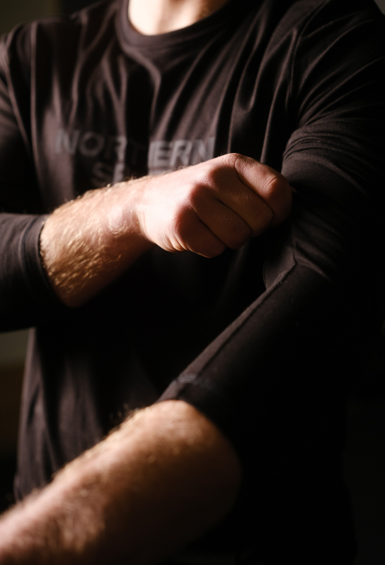 Close-up of a male athlete rolling up the sleeve of a black Northern Spirit long sleeve shirt – minimalist and functional CrossFit apparel.