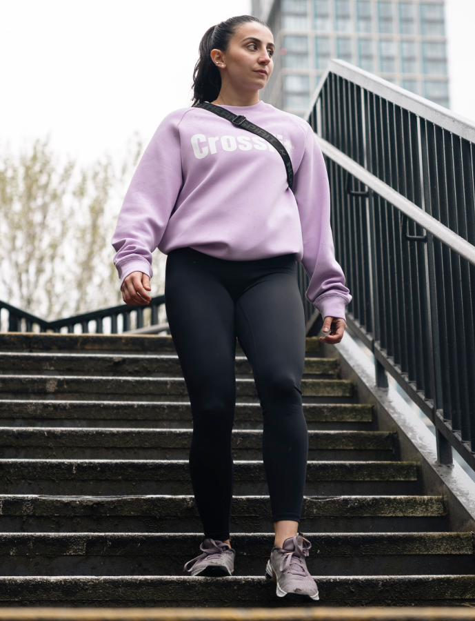 Woman in a purple sweatshirt with 'Crush' text, black leggings, and gray shoes walking up stairs outdoors.