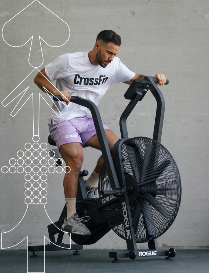 Male athlete training on Echo Bike wearing Northern Spirit CrossFit® white T-shirt and lilac shorts during the Men’s Sale campaign.
